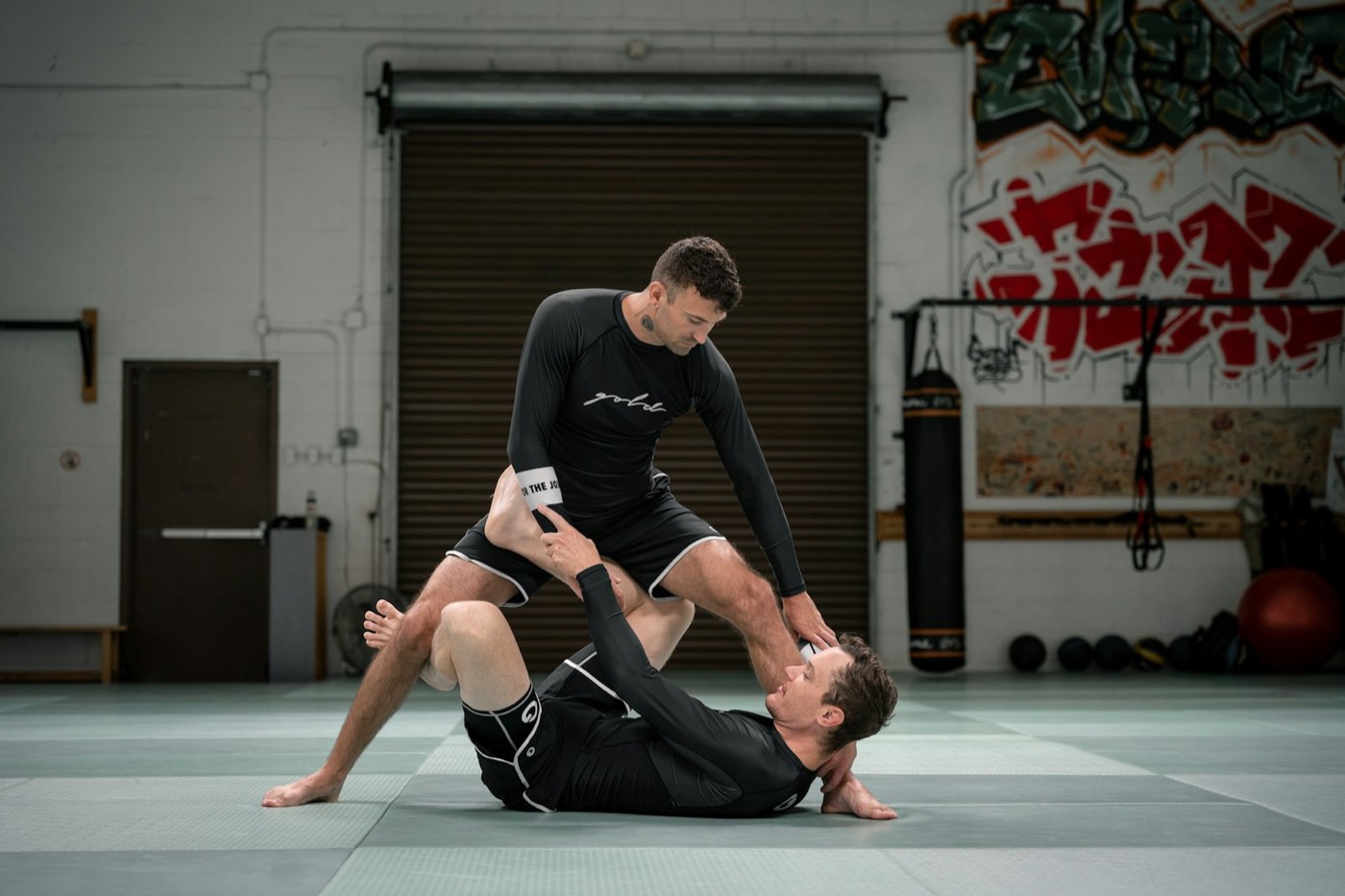 Dois atletas de no-gi treinando passagem de guarda em uma academia